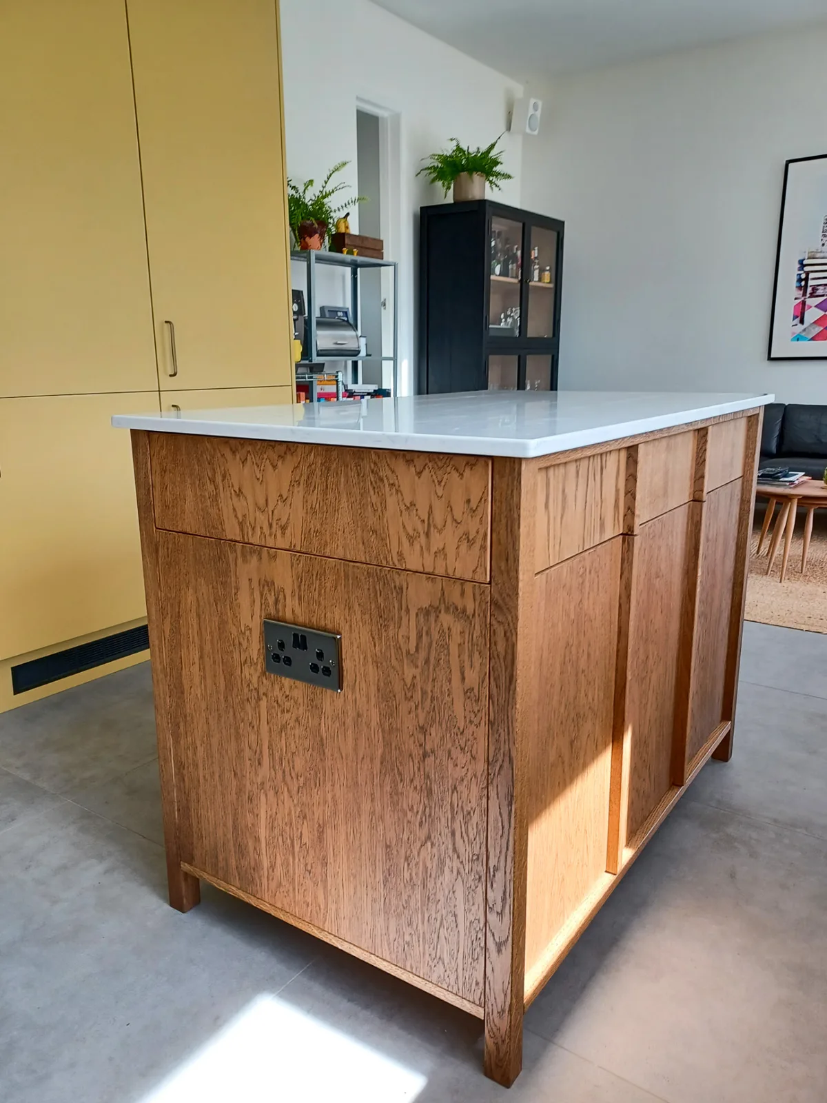 Handmade timber kitchen island with a pale worktop, integrated sockets and yellow cabinetry in an open-plan Wiltshire kitchen