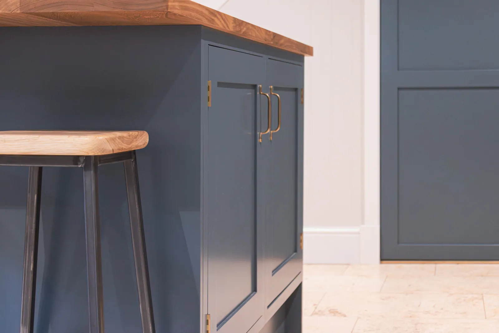 Detail of a navy blue painted kitchen island with solid timber top and a stool