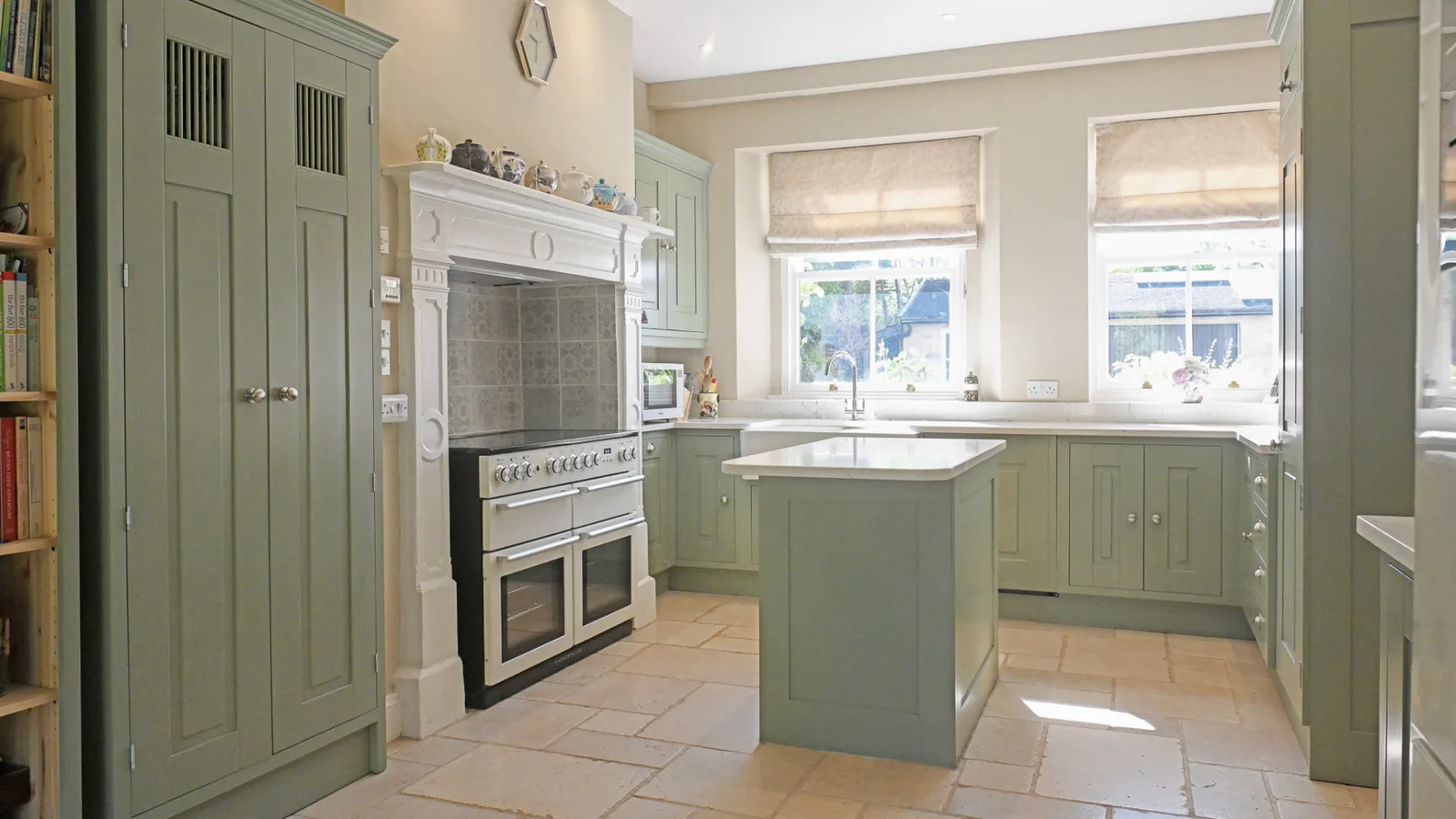 Sage green painted shaker kitchen in Wiltshire with a small island, quartz worktops, range cooker and stone flagstone floor