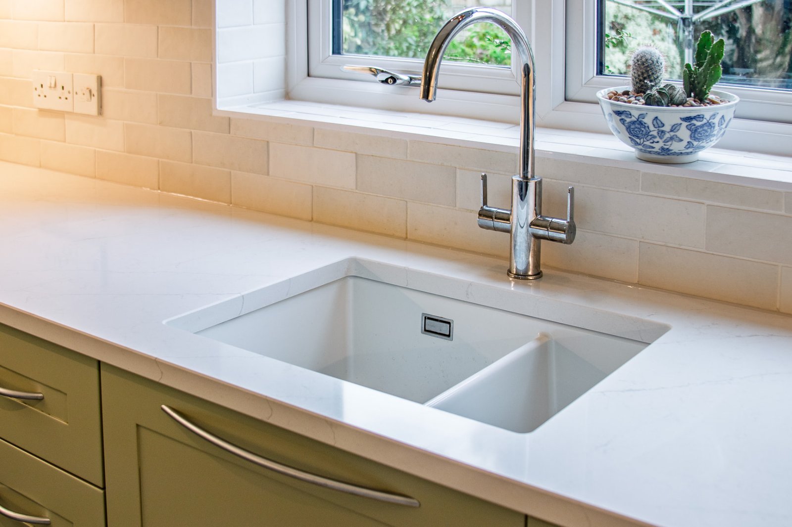 White quartz worktop with an undermount sink and chrome tap beneath a kitchen window
