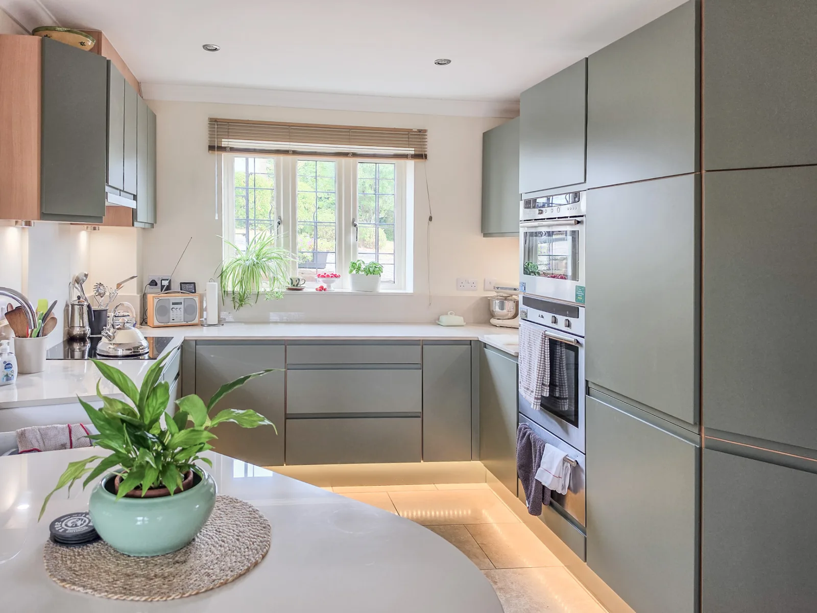 The finished Brinkworth kitchen with handleless green units, a central run of drawers and a bright window