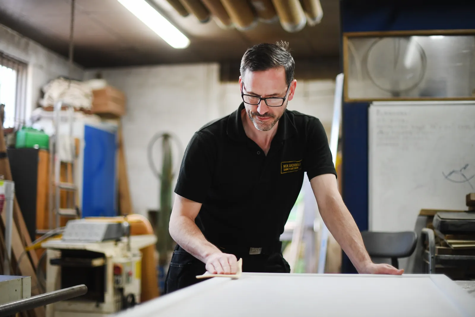 Nick Archibold sanding a cabinet panel at the bench in his Corsham workshop