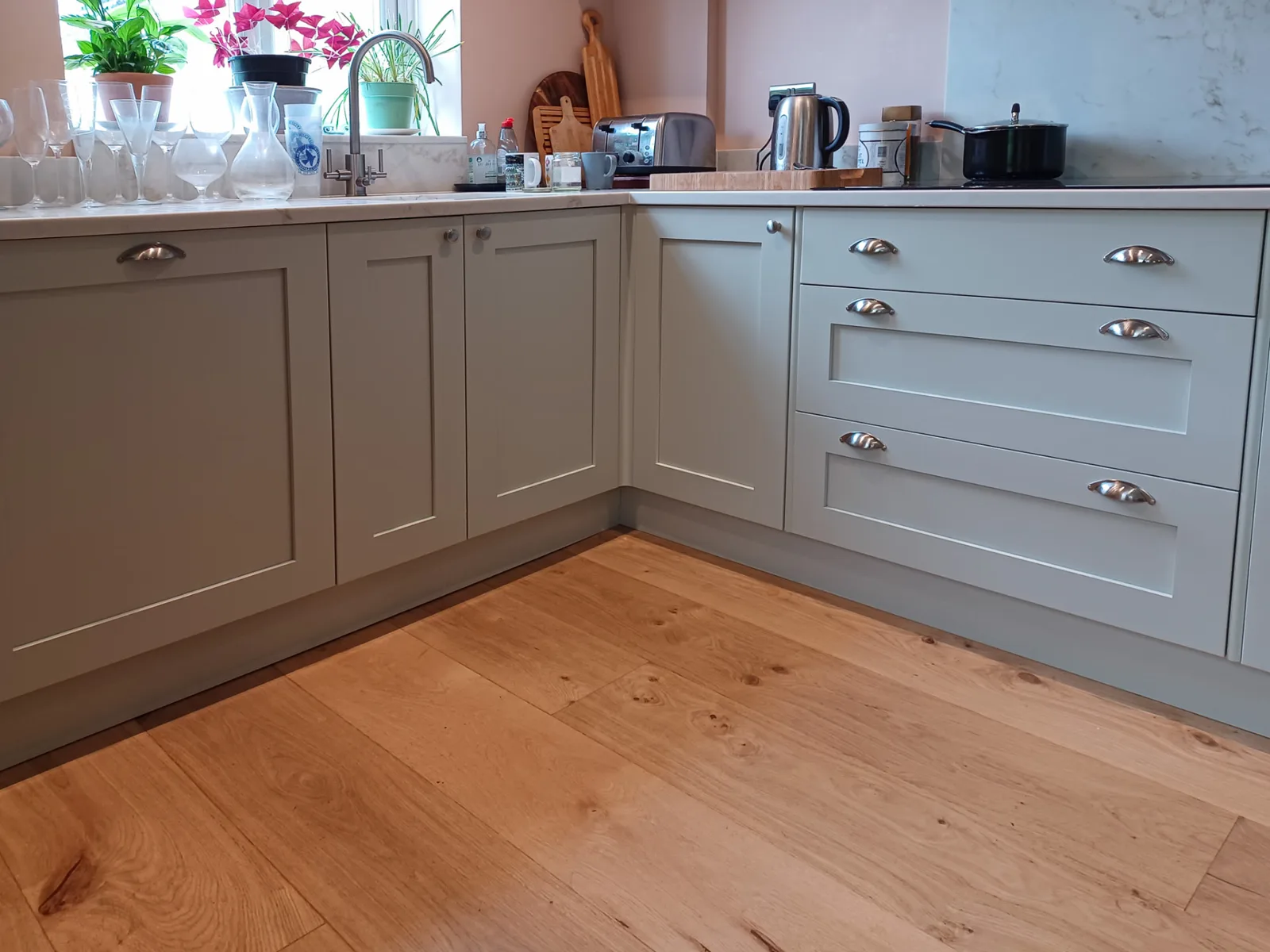 Painted shaker base cabinets with cup handles and pale worktops above a wooden floor in a Wiltshire kitchen