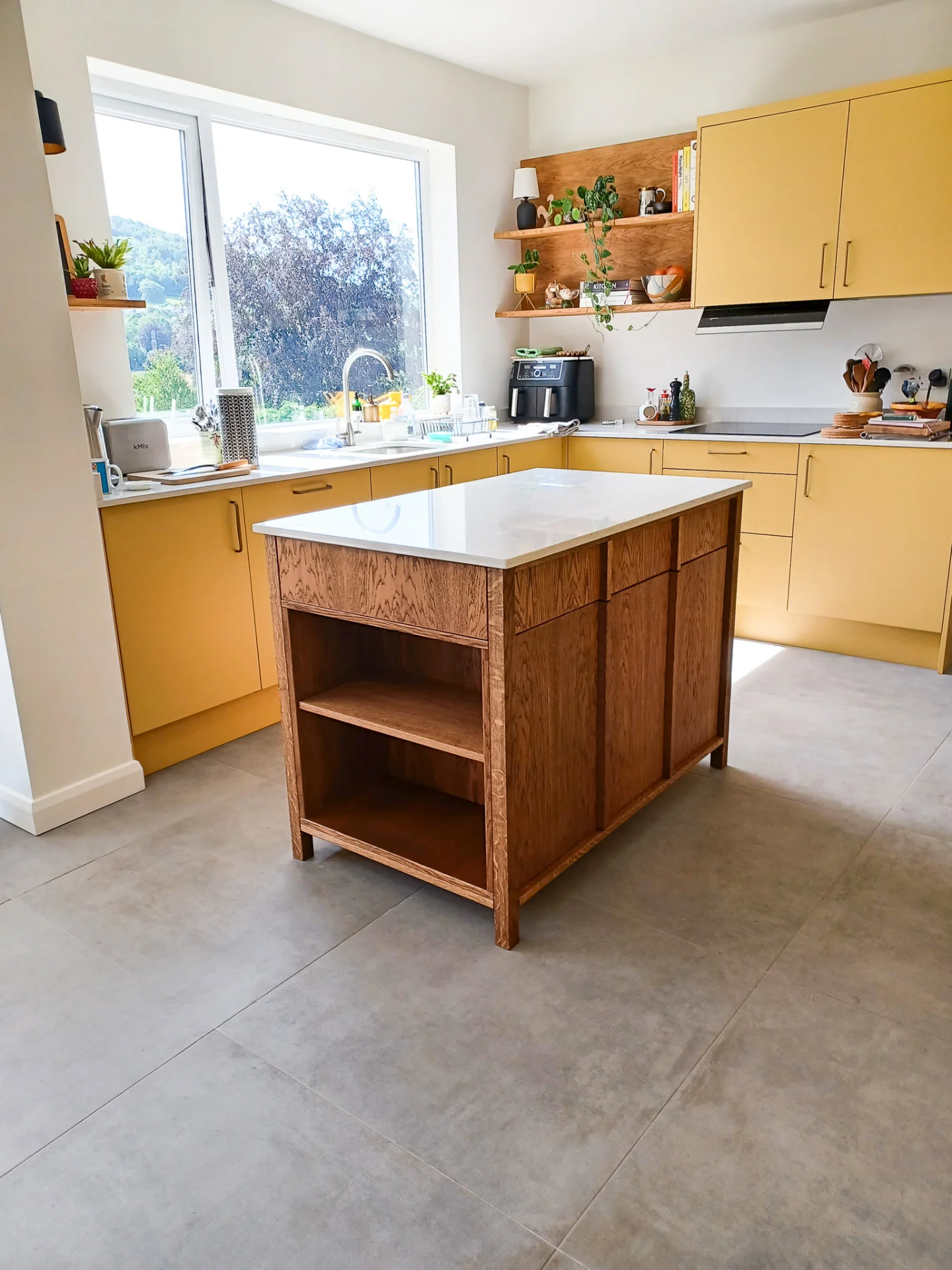 Bespoke solid oak kitchen island with open shelving and a light worktop in a yellow kitchen