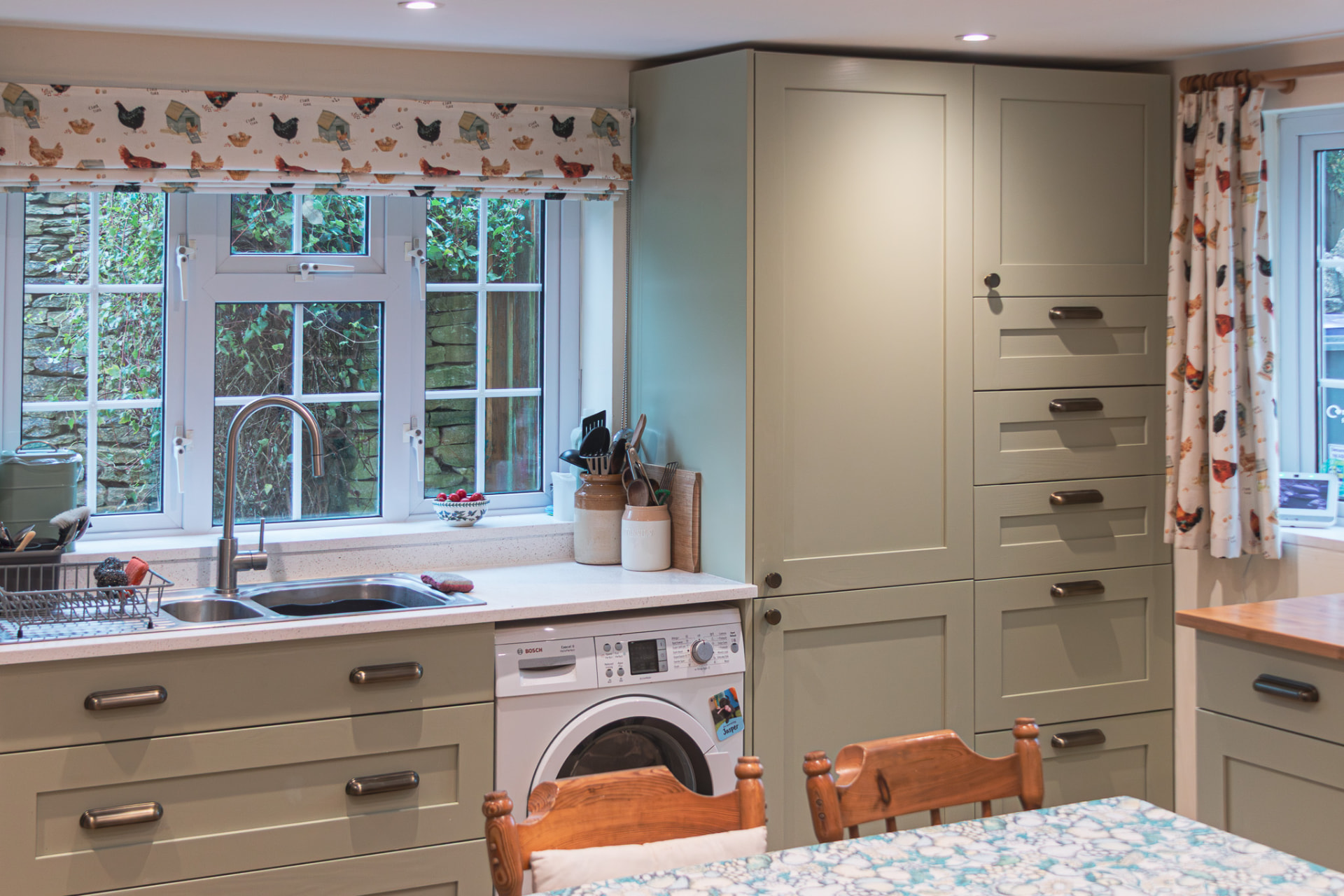 Fitted bespoke painted cabinetry with a sink, washing machine and window in a Wiltshire kitchen