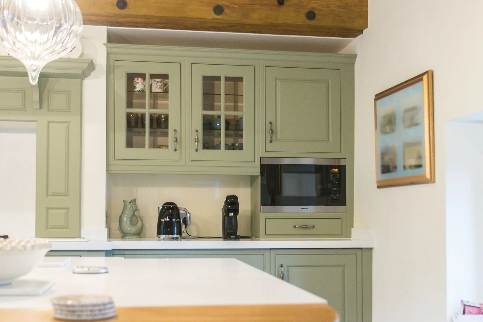 Sprayed glazed wall cabinets in sage green beside a built-in microwave, in Bradford on Avon