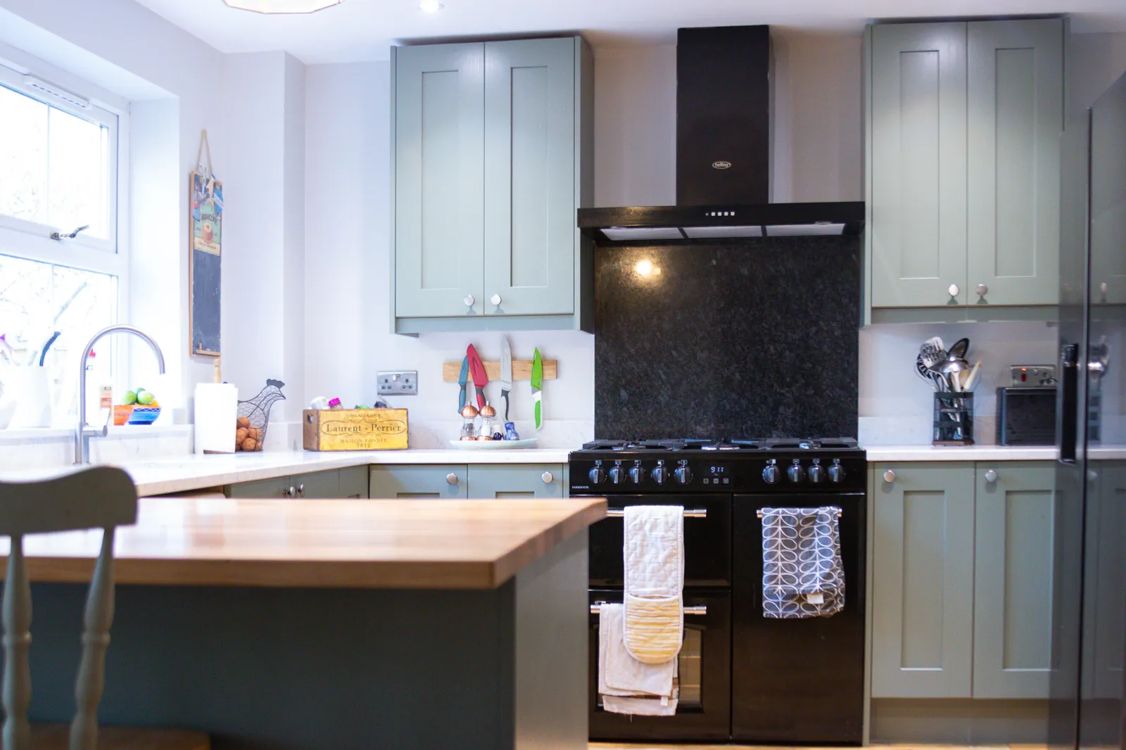 Sage green shaker kitchen with a black range cooker and cooker hood in a Corsham home