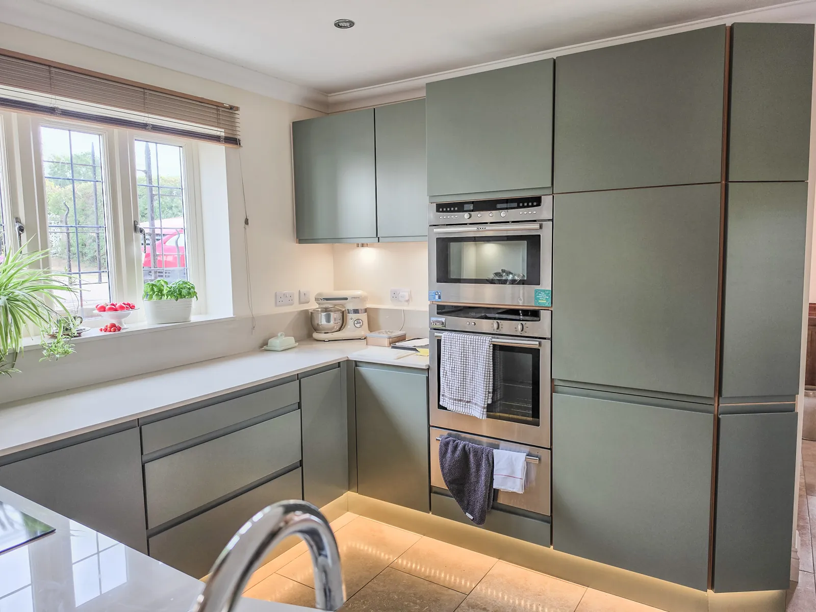 Finished Brinkworth kitchen with green handleless doors, white worktops and illuminated plinths