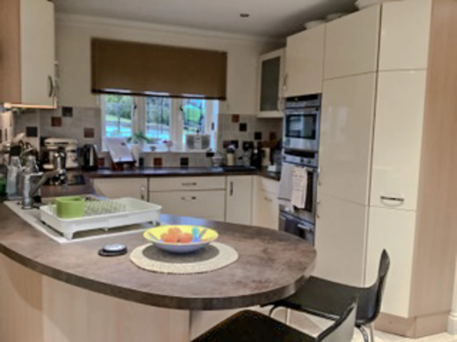 The Brinkworth kitchen before its refresh, with cream vinyl-wrapped slab doors, dark laminate worktops and a curved peninsula with two bar stools