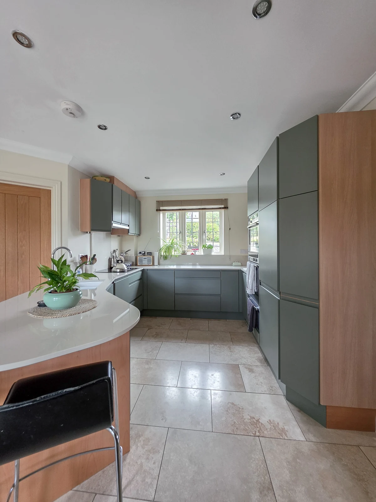 The refreshed Brinkworth kitchen, with mid-green handleless J-pull doors, pale cream Dekton worktops and a curved peninsula