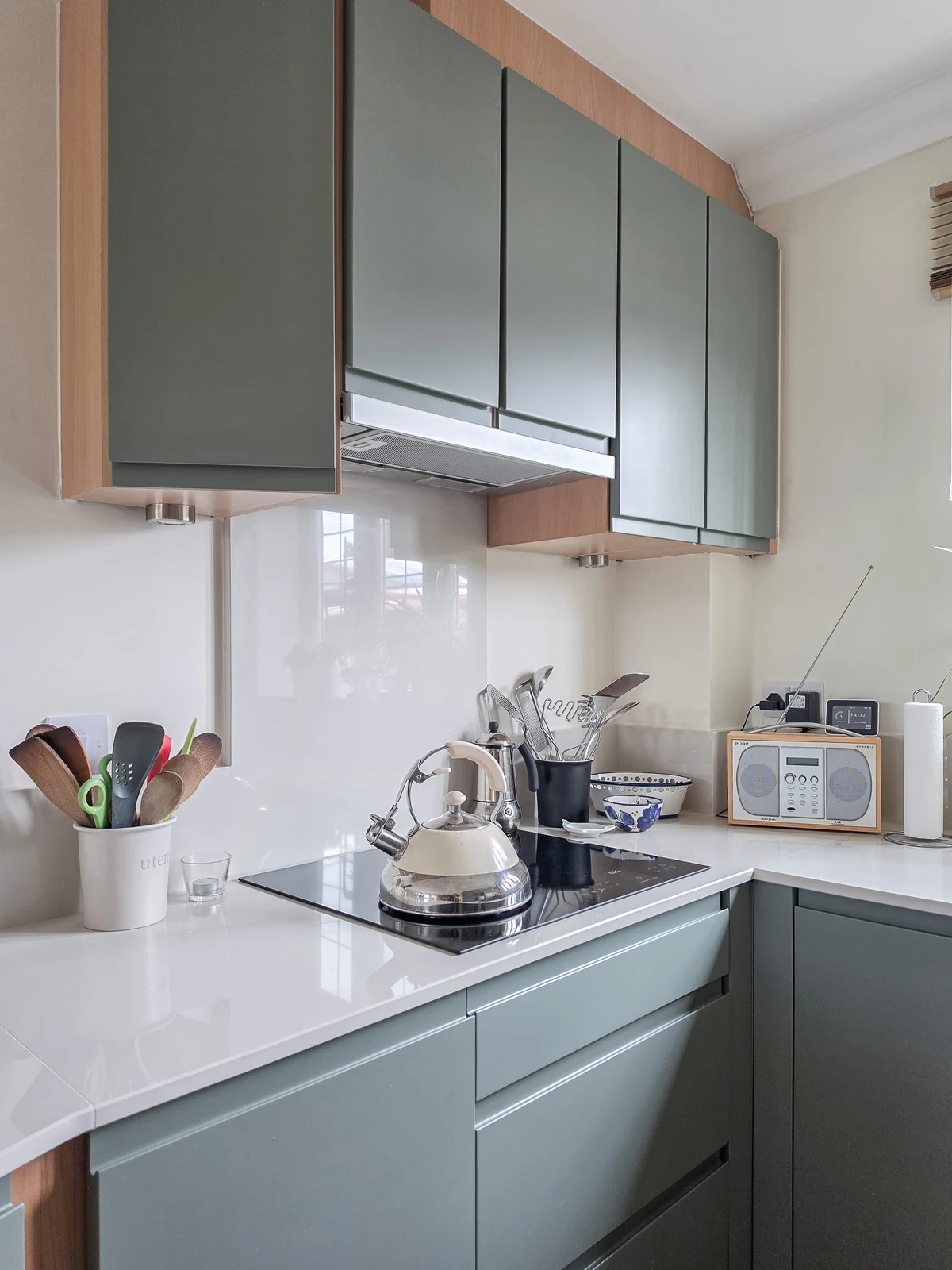 The hob area of the refreshed Brinkworth kitchen, with mid-green J-pull doors framed in steamed beech, an induction hob and under-cabinet lighting
