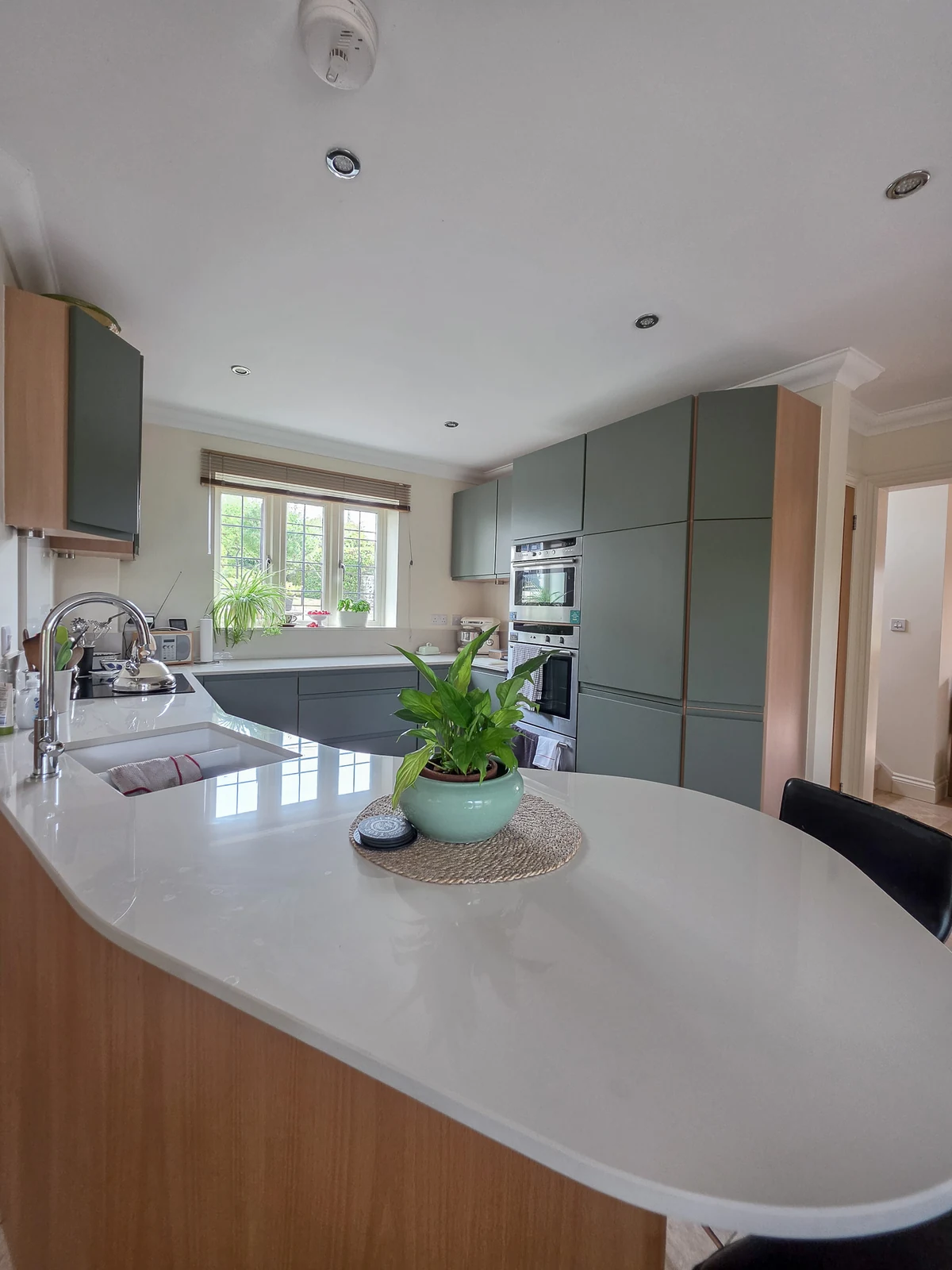 The angled peninsula and breakfast bar in the refreshed Brinkworth kitchen, with a pale cream Dekton worktop and an undermount sink beneath the window