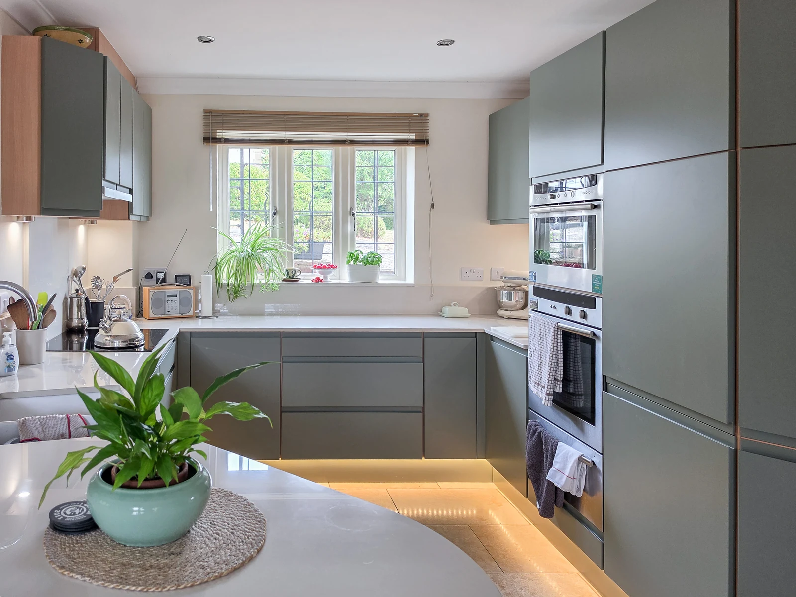 The refreshed Brinkworth kitchen with mid-green handleless J-pull doors, pale cream Dekton worktops and new under-cabinet and plinth LED lighting