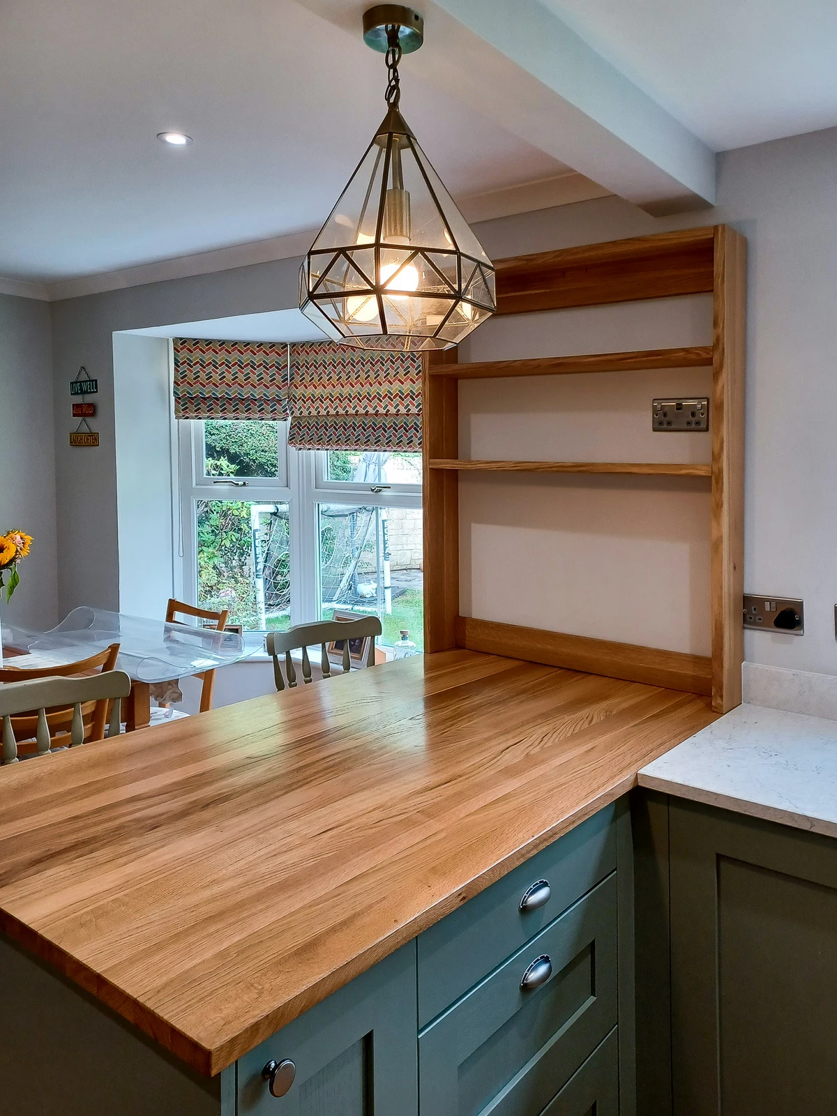 The solid oak worktop on the peninsula beside the workshop-made oak shelving unit in the Corsham custom kitchen, looking through to the dining table
