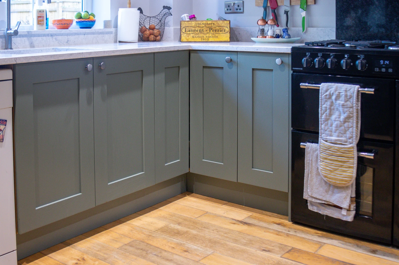 The practical zone of the Corsham custom kitchen, with the ceramic undermount sink and black range cooker beneath Regiment Green shaker cabinets and a white quartz worktop