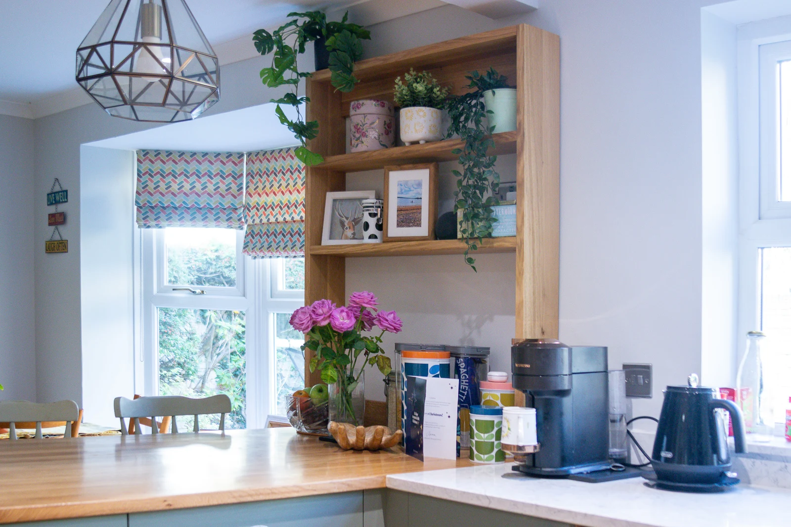 The bespoke solid oak shelving unit at the end of the peninsula in the Corsham custom kitchen, holding display pieces with the white quartz worktop and Regiment Green cabinetry behind