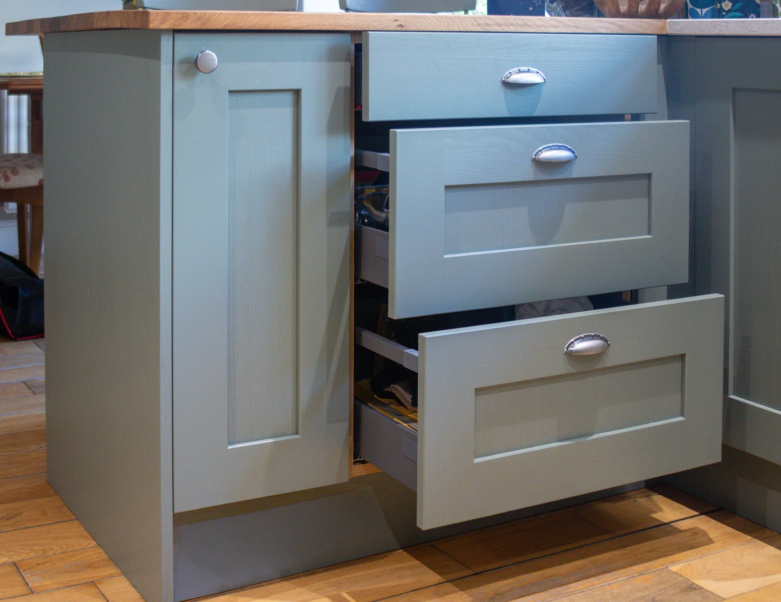 Drawers pulled open in the Corsham custom kitchen showing organised internal storage, with the solid oak worktop meeting the white quartz at the corner