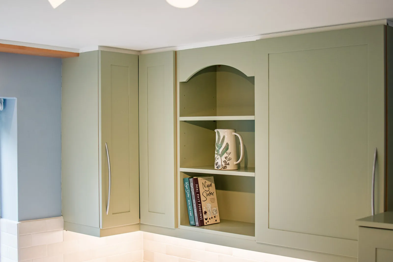 Sage green shaker wall cabinets with an open display shelf in a refreshed Wiltshire kitchen