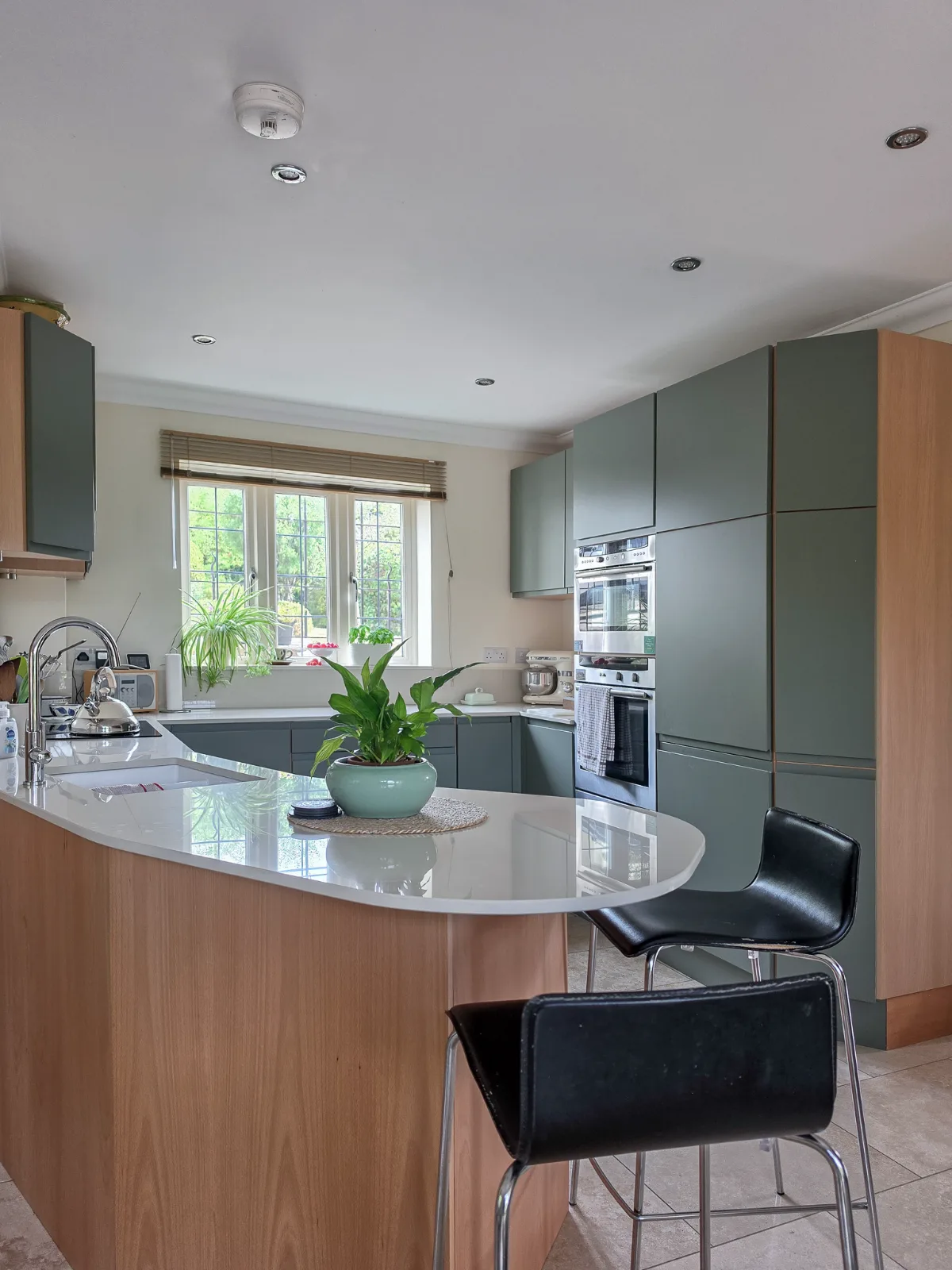 A curved breakfast bar with a pale worktop, timber panels and green kitchen cabinets.