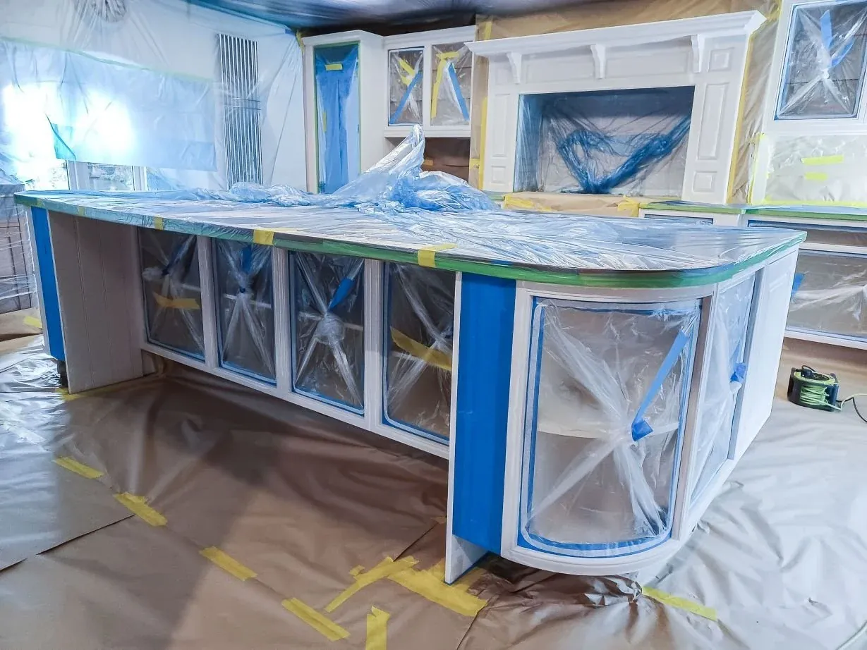 The island and fixed cabinetry fully masked with film and tape, floors protected, ready for spraying in place