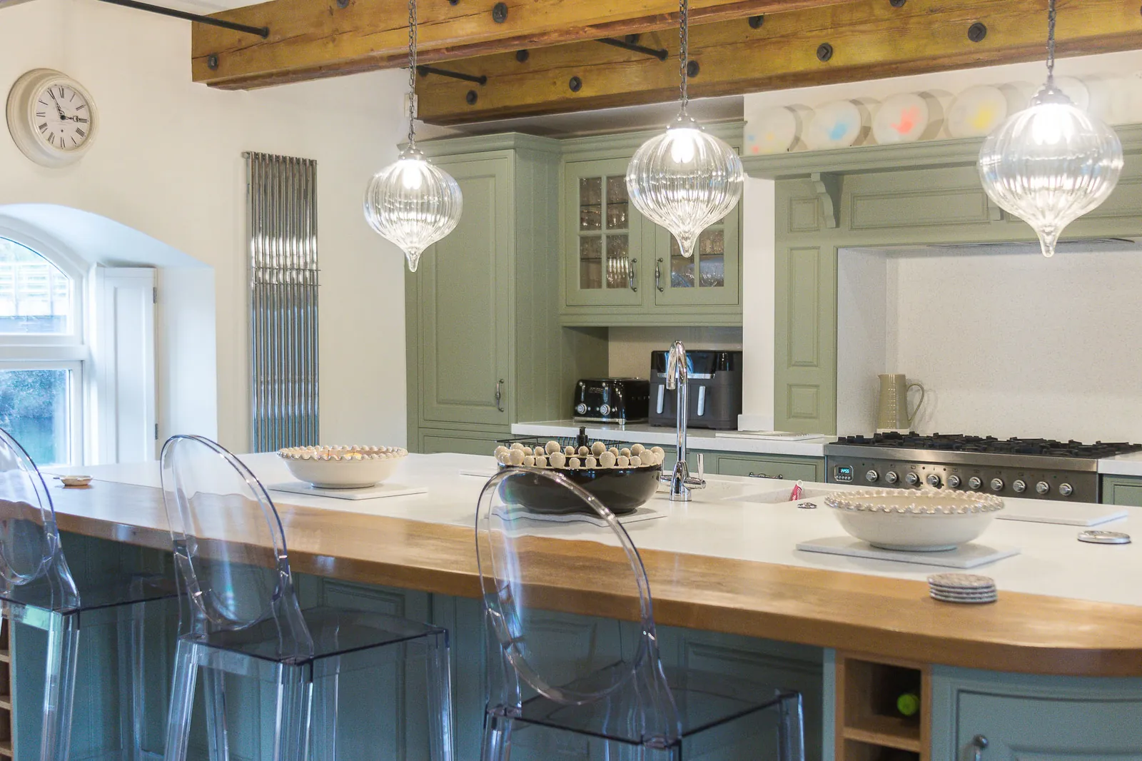 Wide view across the island towards the green-painted cabinetry, glazed cupboard and range-cooker alcove