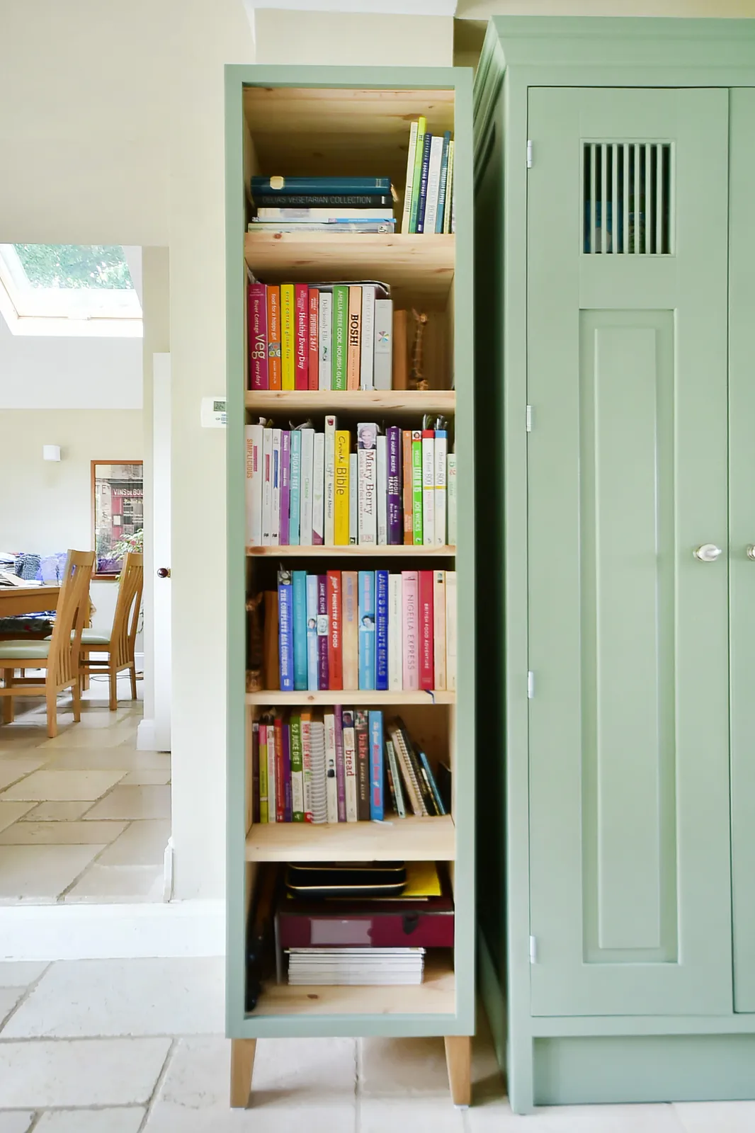 A tall bespoke bookcase in green with pine shelves beside a larder cupboard