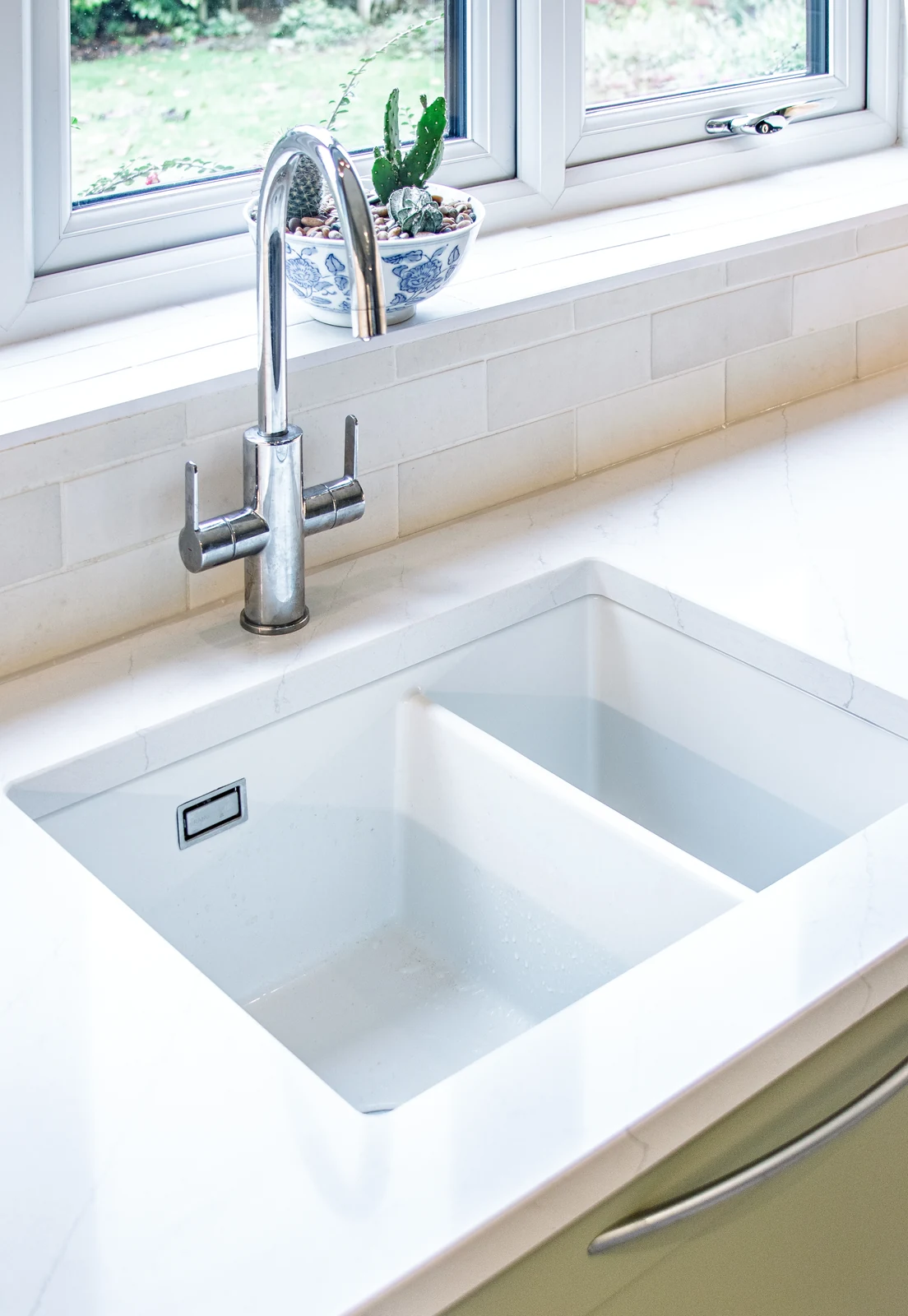 Close view of the ceramic undermount sink in the lightly-veined quartz worktop, with the existing tiled splashback and garden windowsill behind